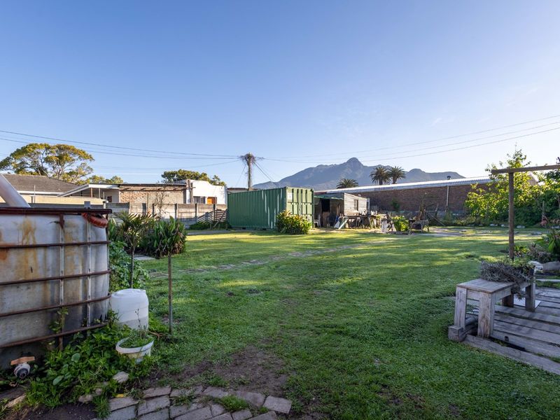 Spacious rear garden area featuring a lawn, boundary walling, and mountain views, offering significant potential for landscaping and outdoor development.