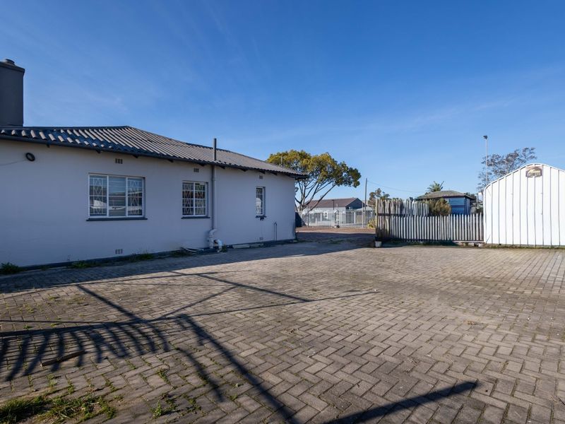 Rear exterior view of the commercial property featuring a paved yard, security fencing, and a detached metal storage shed.