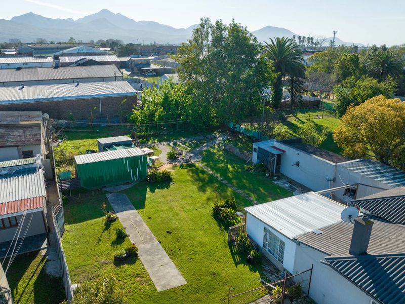 Aerial view of a commercial property lot featuring multiple structures with corrugated metal roofing, a central lawn, and surrounding industrial buildings.