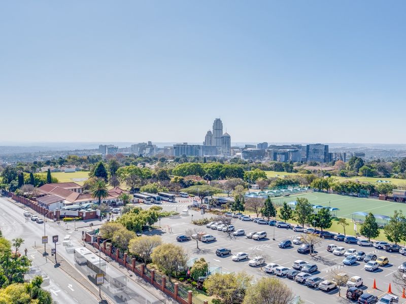 Elevated panoramic view overlooking the surrounding urban landscape, including nearby sports fields, parking facilities, and the distant city skyline.