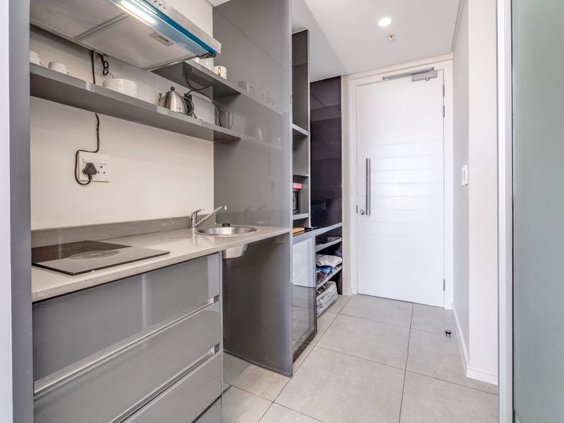 Compact modern kitchen featuring grey high-gloss cabinetry, stone countertops, integrated hob, extractor fan, and tiled flooring.
