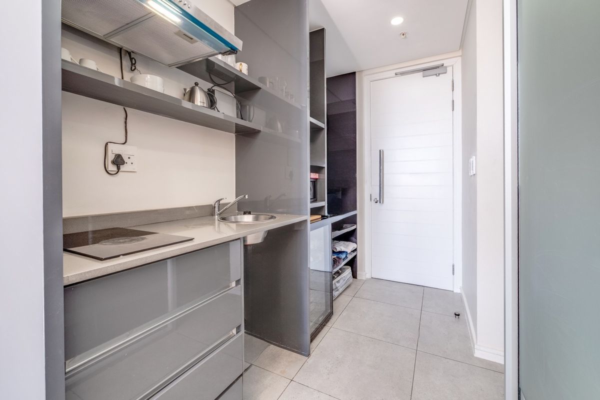 Compact modern kitchen featuring grey high-gloss cabinetry, stone countertops, integrated hob, extractor fan, and tiled flooring.
