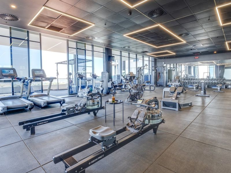 Modern, well-equipped fitness center featuring floor-to-ceiling windows, professional rubber flooring, mirrored walls, and integrated recessed LED lighting.