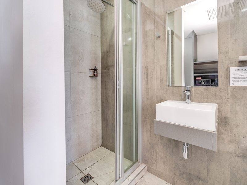 Modern bathroom featuring a glass-enclosed shower with a rain shower head and a sleek wall-mounted basin with chrome fixtures.