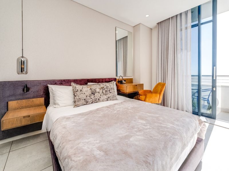 Modern bedroom featuring a built-in headboard, floating bedside table, and large sliding glass doors leading to a private balcony with natural light.