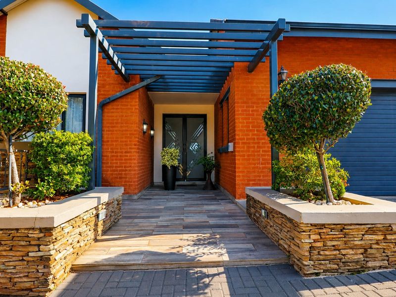 A well-maintained front entrance featuring a modern pergola, stone-clad planter boxes, and a tiled walkway leading to a stylish double front door.