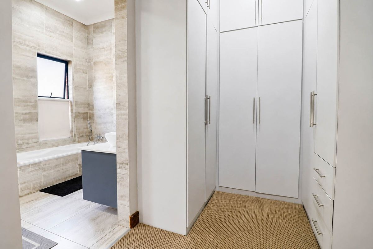 A spacious bedroom area featuring extensive built-in cupboards and an open-plan transition to a modern tiled bathroom with a built-in bathtub and vanity.