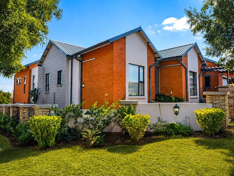 A well-maintained modern house exterior featuring a combination of brick and panelled cladding, metal roofing, and stone-accented boundary walls with landscaped garden.