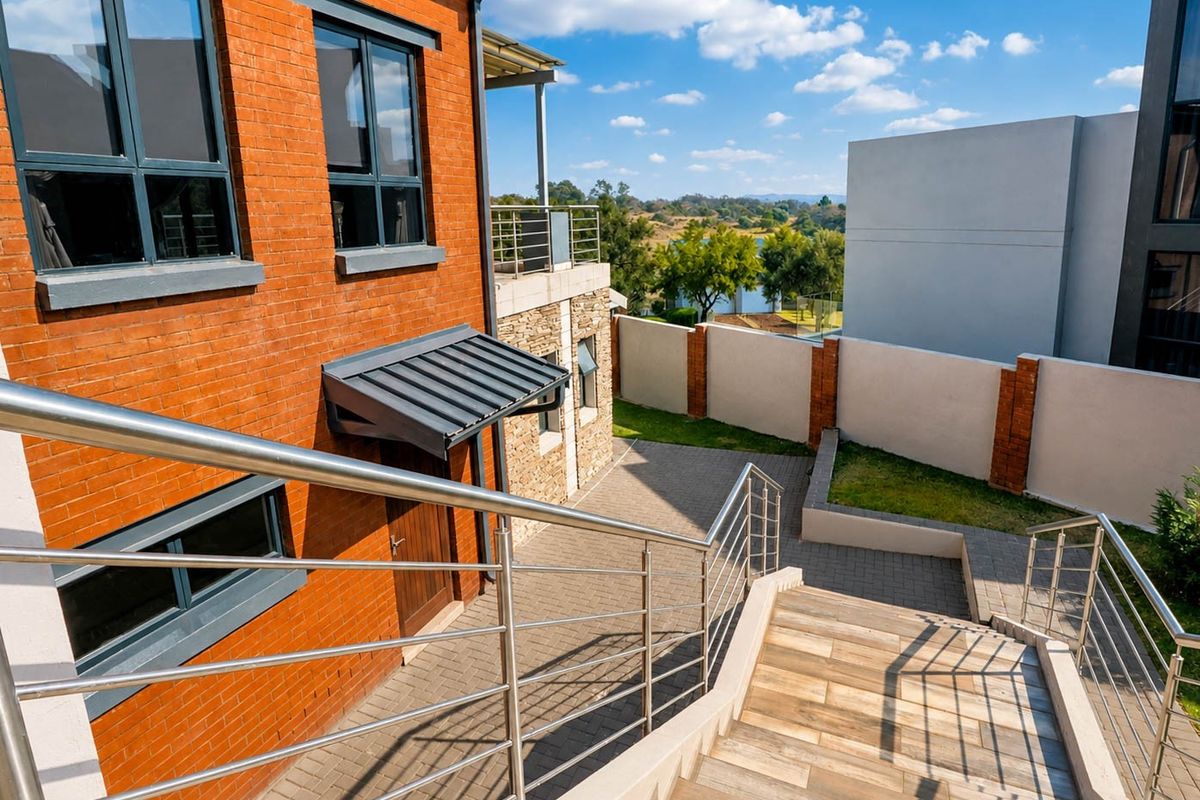 A well-maintained rear exterior featuring a brick facade, modern stainless steel balustrades, tiled staircase, and a paved courtyard area with boundary walling.