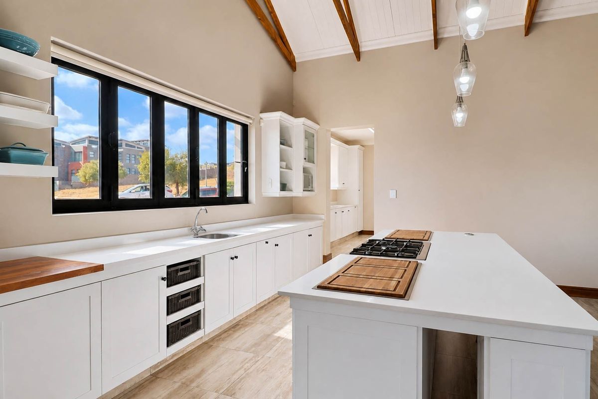 Modern kitchen featuring a large central island with a built-in gas hob, white shaker cabinetry, vaulted ceilings with exposed timber rafters, and ample natural light.