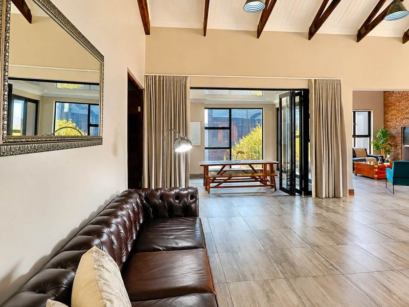 Spacious open-plan living area featuring vaulted ceilings with exposed timber beams, tiled flooring, and bi-fold doors leading to an outdoor patio space.
