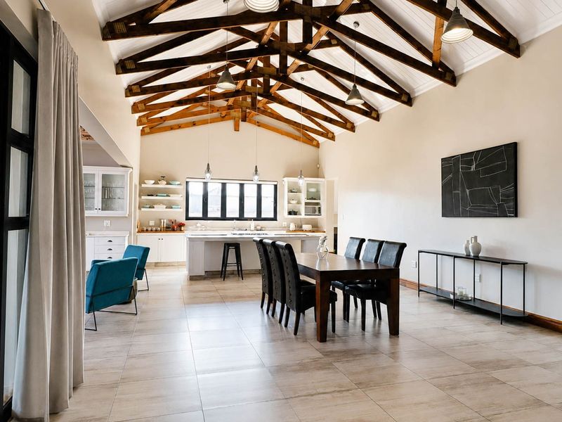 Spacious open-plan living and dining area featuring a striking vaulted ceiling with exposed timber trusses, tiled floors, and a modern kitchen island.
