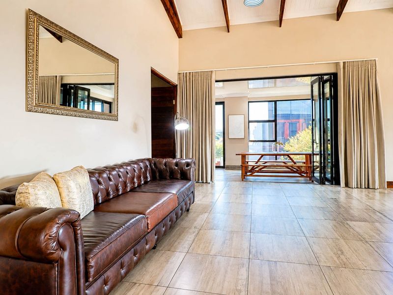 Spacious living area featuring vaulted ceilings with exposed timber beams, large format tiled flooring, and bi-fold doors opening to an outdoor patio space.