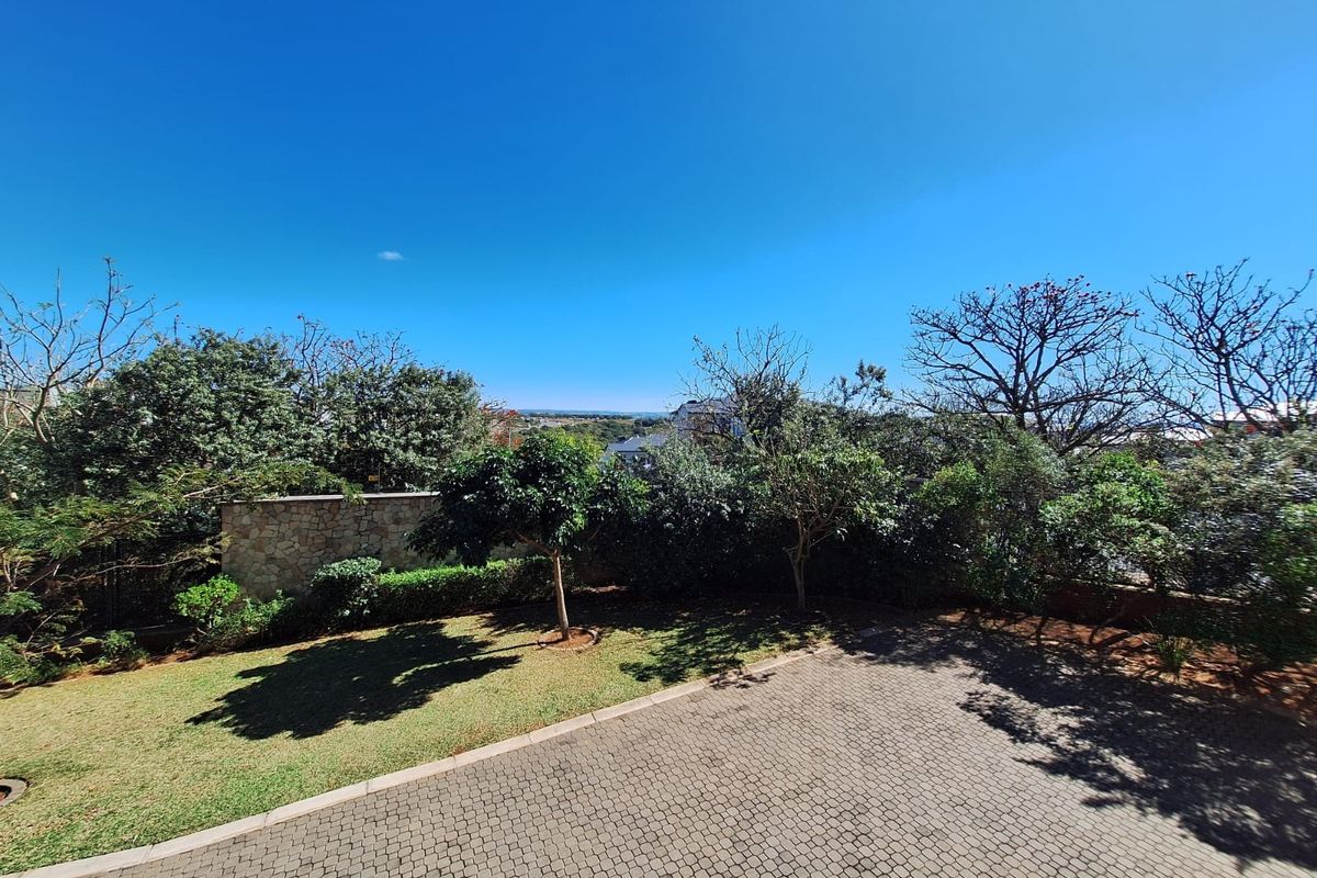 A well-maintained rear garden area featuring a paved driveway, established trees, and a stone boundary wall with distant landscape views.