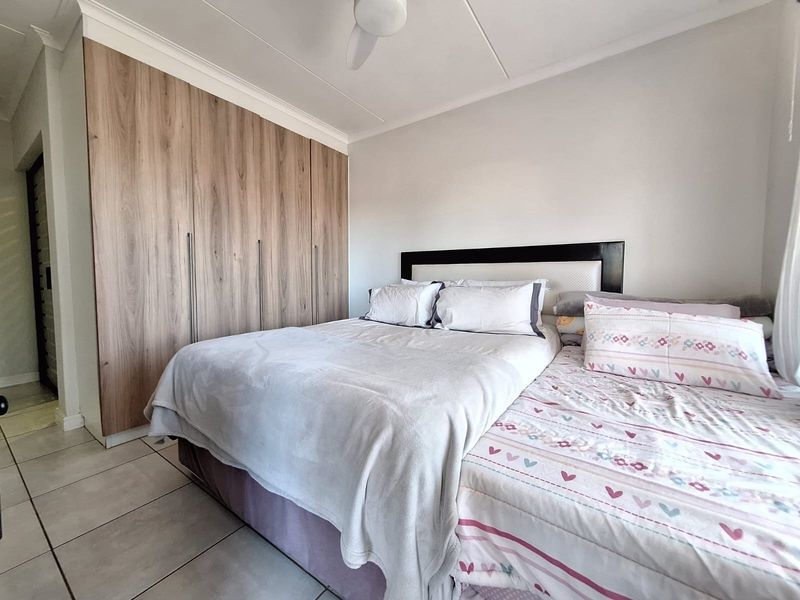 A well-maintained bedroom featuring modern wood-finish built-in cupboards, a ceiling fan, and neutral tiled flooring.