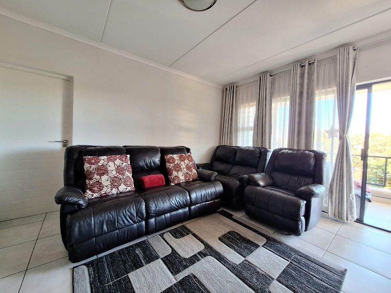 A bright living room featuring neutral tiled flooring and a large sliding glass door providing access to an outdoor balcony area.