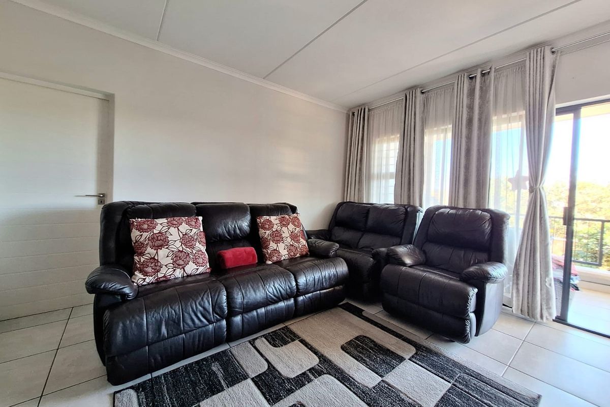 A bright living room featuring neutral tiled flooring and a large sliding glass door providing access to an outdoor balcony area.
