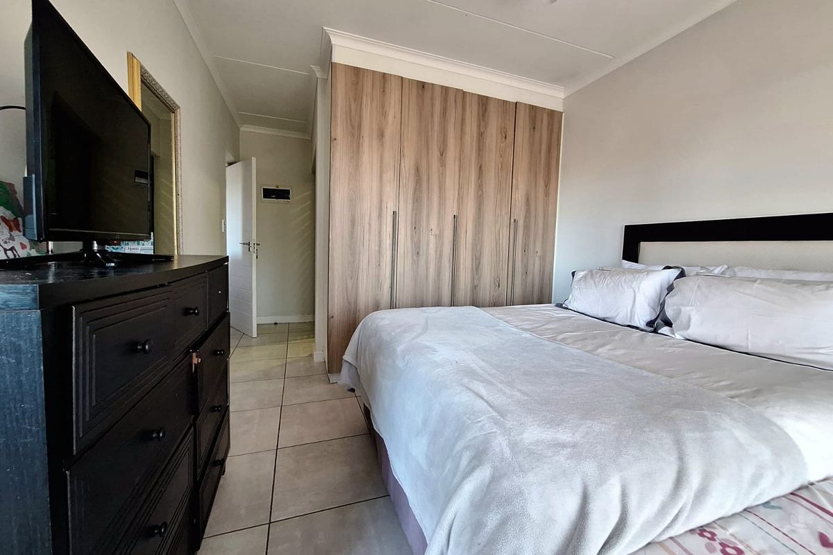 A well-maintained bedroom featuring neutral tiled flooring, modern wood-finish built-in cupboards, and a ceiling fan.