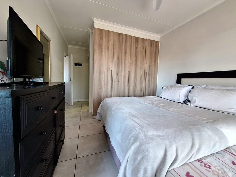 A well-maintained bedroom featuring neutral tiled flooring, modern wood-finish built-in cupboards, and a ceiling fan.