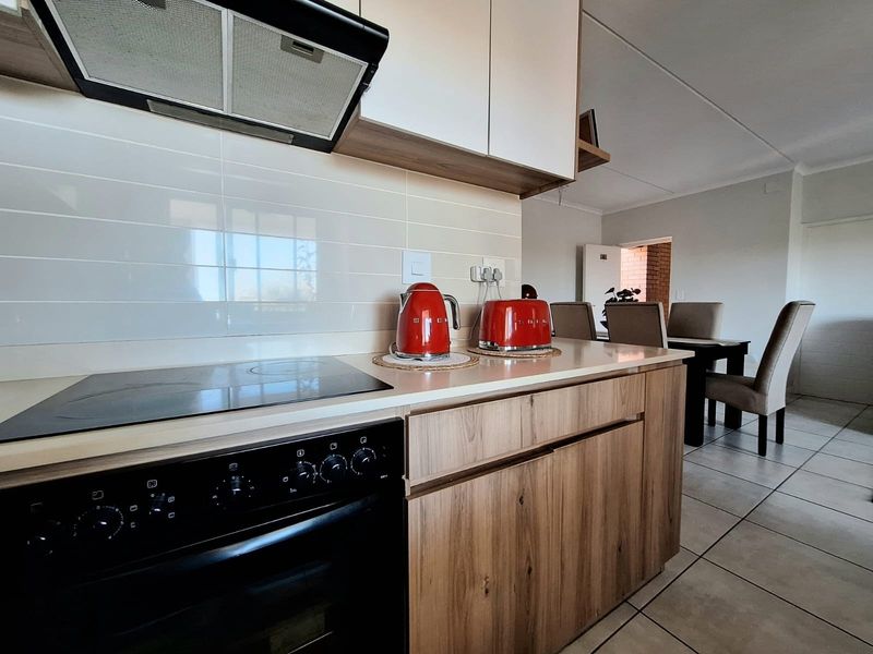 Modern open-plan kitchen featuring wood-finish cabinetry, integrated electric hob, oven, and extractor fan, seamlessly flowing into the adjacent dining area.