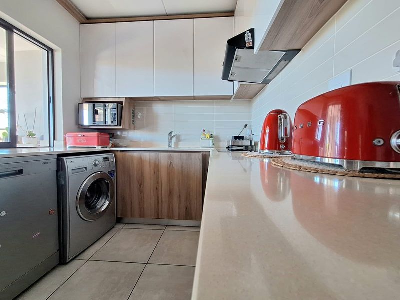 Modern kitchen featuring sleek white and wood-grain cabinetry, stone countertops, subway tile backsplash, and integrated extractor fan with tiled flooring.