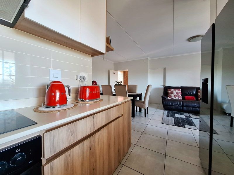 Modern open-plan kitchen and living area featuring wood-finish cabinetry, stone countertops, and tiled flooring, creating a seamless flow between cooking and lounge spaces.