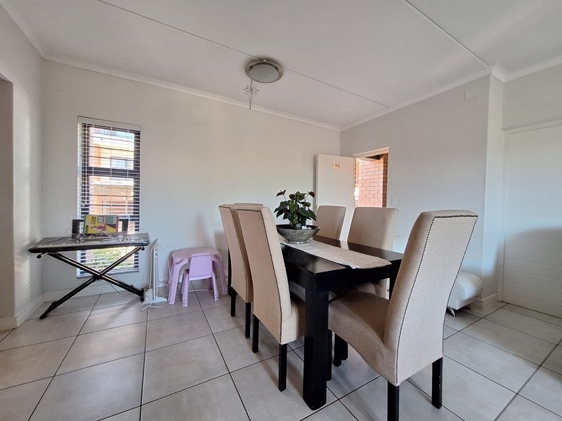 A functional dining area featuring neutral tiled flooring, a central ceiling light, and a window fitted with venetian blinds.