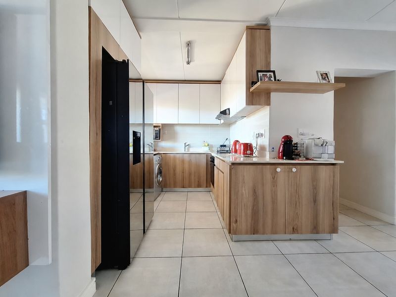 Modern kitchen featuring wood-grain and white cabinetry, tiled flooring, integrated appliance spaces, and a functional layout with ample counter space.
