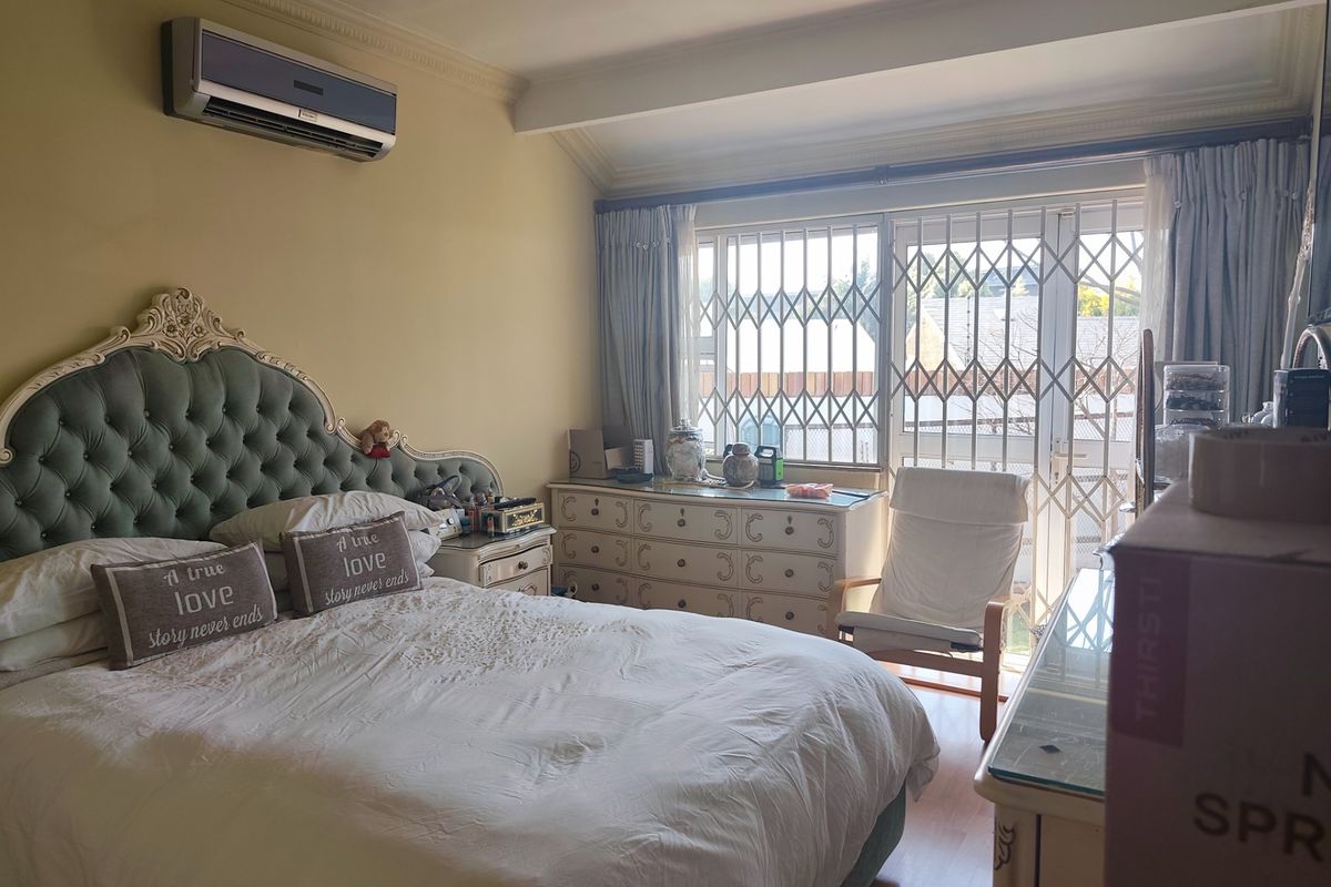 A bedroom featuring laminate flooring, a wall-mounted air conditioning unit, and a sliding glass door with an integrated security gate leading to the exterior.