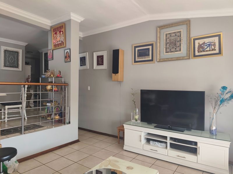 A well-maintained living room featuring tiled flooring, crown molding, and a modern stainless steel balustrade overlooking an adjacent lower level.