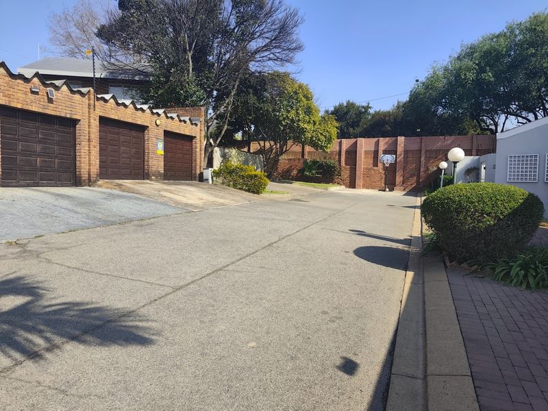 A view of the property frontage featuring a triple garage, paved driveway, and secure brick boundary walling.
