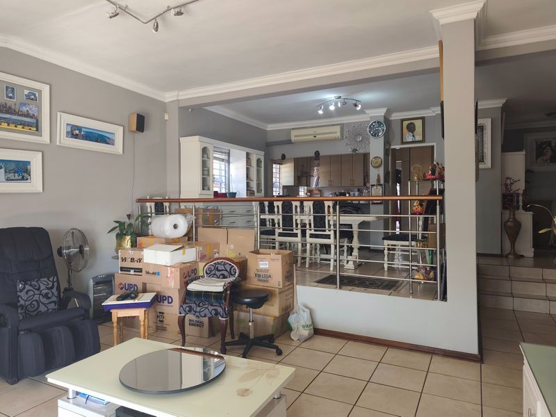 An open-plan living and dining area featuring ceramic tiled flooring, coved cornicing, and a split-system air conditioner, with a raised dining platform and stainless steel balustrade.