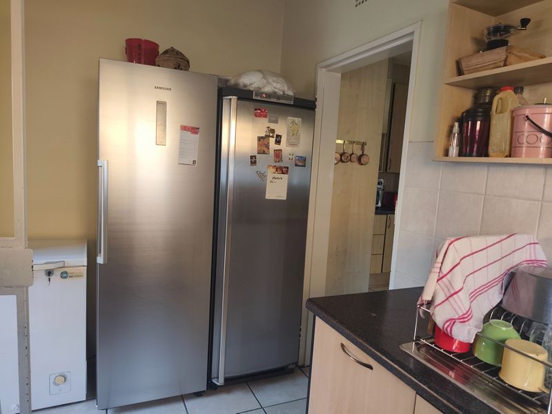 A functional scullery area featuring laminate cabinetry, tiled backsplash, and tiled flooring, providing additional storage and prep space adjacent to the main kitchen.