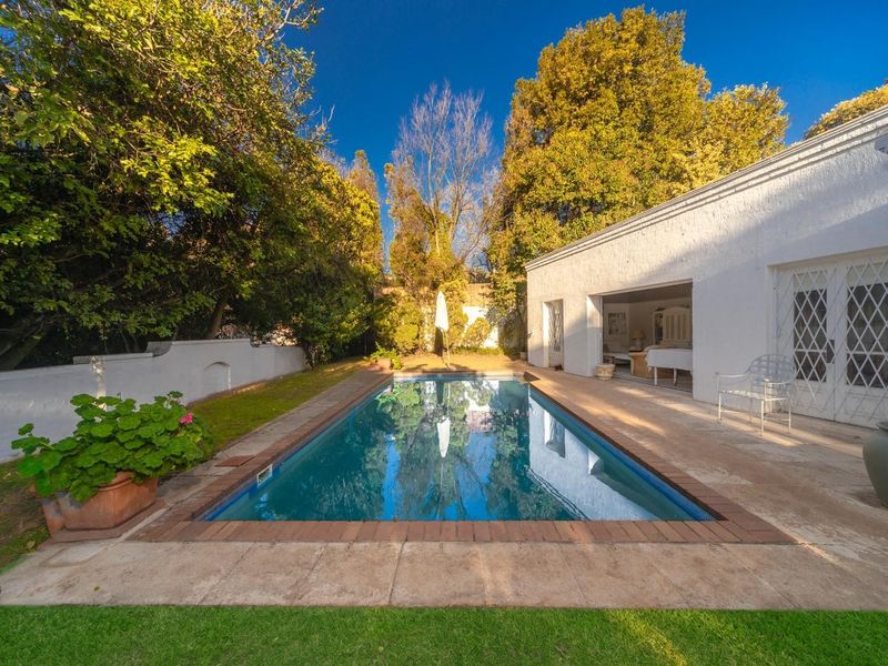 Outdoor pool area featuring a rectangular swimming pool with brick coping, paved surround, and access to the main building via lattice security doors.
