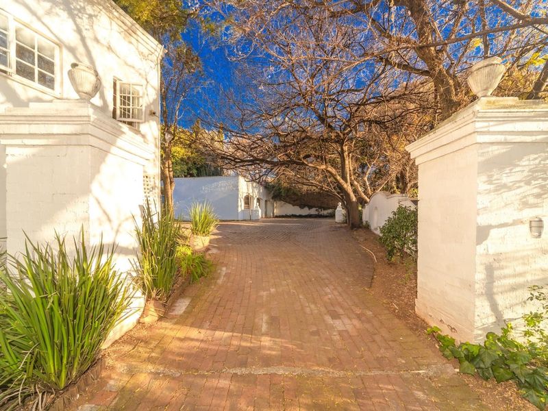 A view of the property entrance featuring a brick-paved driveway flanked by masonry pillars and mature trees.