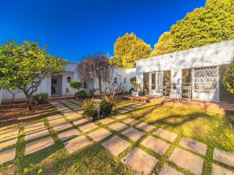 A well-maintained rear courtyard featuring a paved stone walkway, established garden, and direct access to the building via a terrace and security-gated entrance.