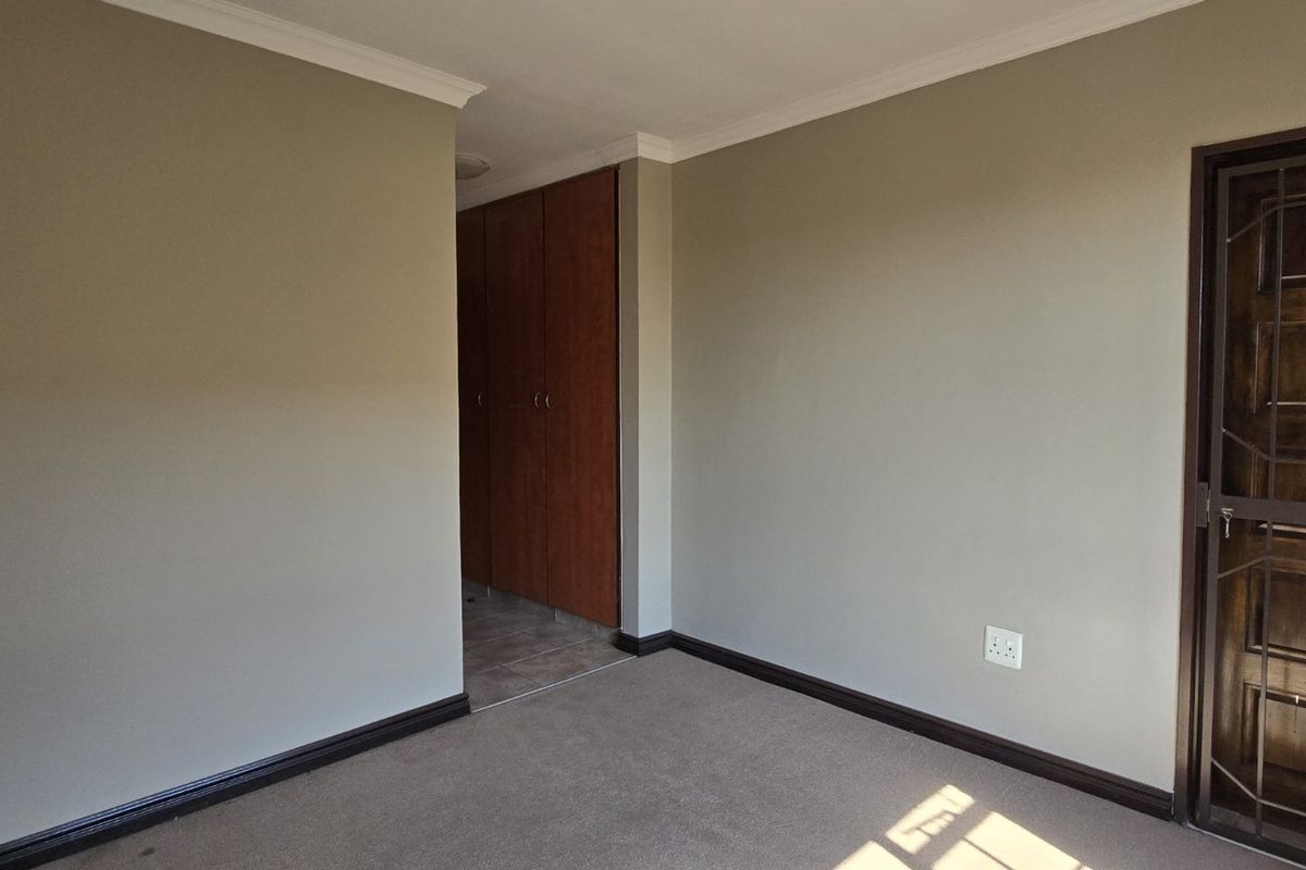 An empty bedroom featuring neutral wall tones, carpeted flooring, built-in wooden cupboards, and a secure metal entrance gate.