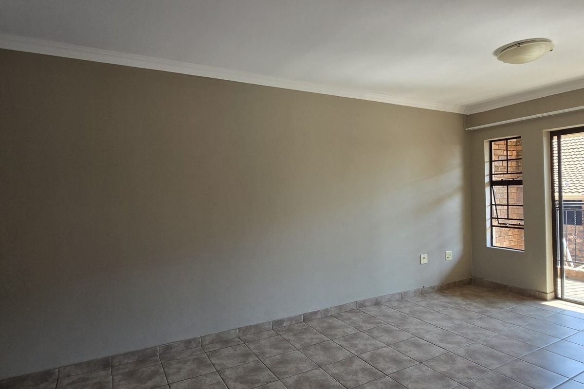 An empty living room featuring tiled flooring, neutral walls, and a sliding glass door providing access to an outdoor balcony area.