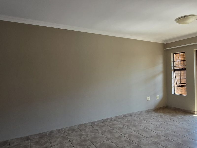 An empty living room featuring tiled flooring, neutral walls, and a sliding glass door providing access to an outdoor balcony area.