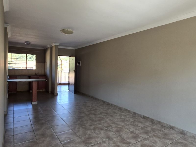 An open-plan living and kitchen area featuring neutral wall tones, tiled flooring, and direct access to an outdoor balcony space.