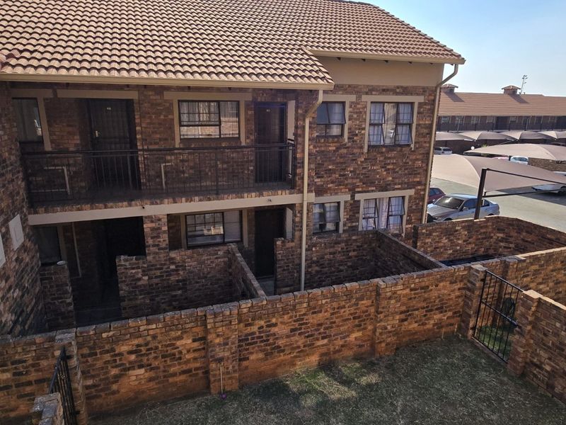 Exterior view of a face brick apartment complex featuring private courtyard walls, a balcony with metal railings, and tiled roofing.