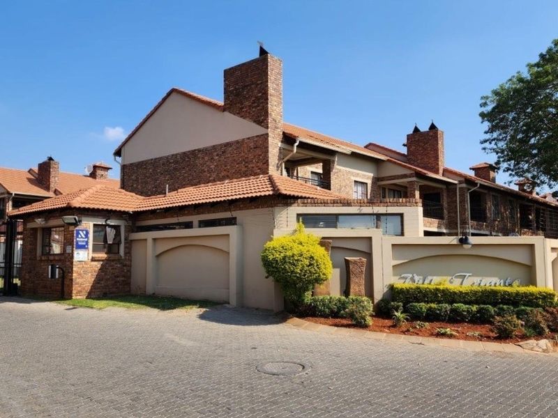 Front exterior view of a face-brick apartment complex featuring a secure gated entrance, paved driveway, and established perimeter walling.