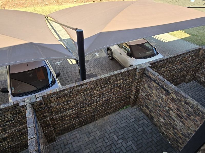 An elevated view of a private paved courtyard area with brick boundary walls, adjacent to a covered parking space with shade sails.