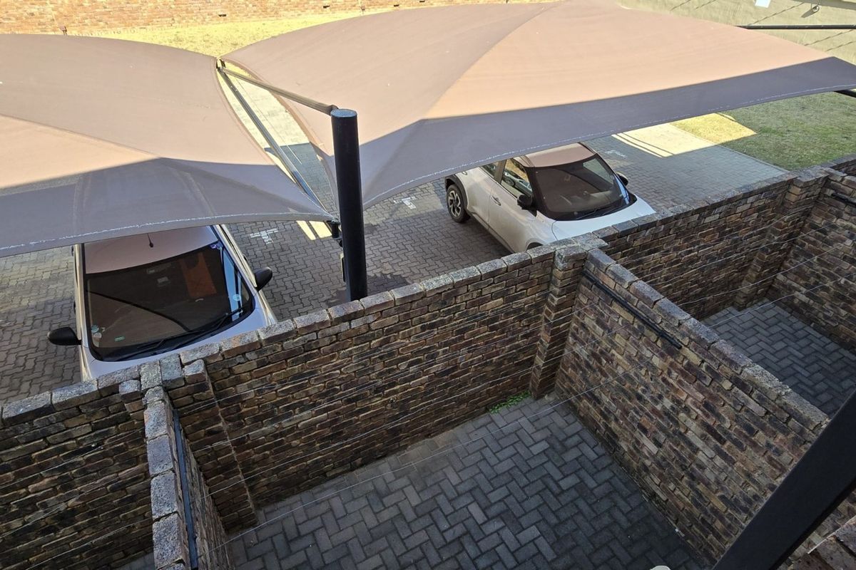 An elevated view of a private paved courtyard area with brick boundary walls, adjacent to a covered parking space with shade sails.