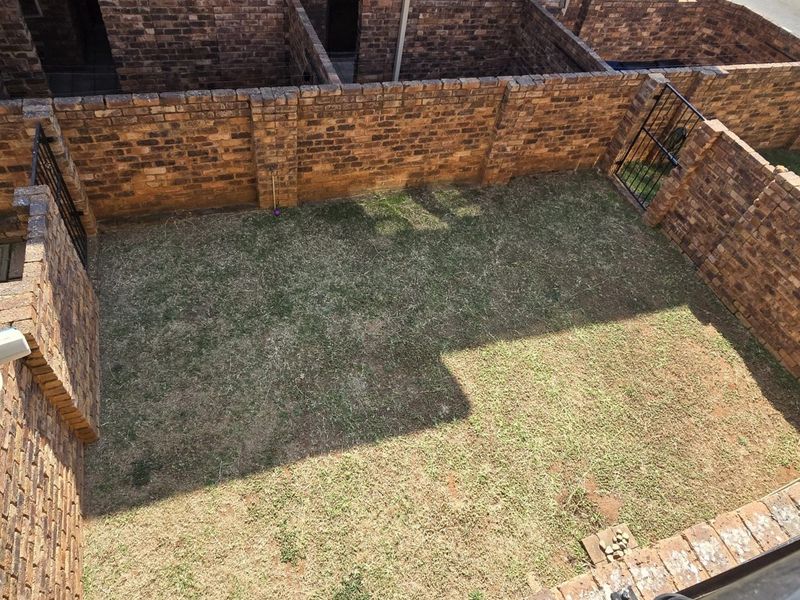 An elevated view of a private rear garden enclosed by face brick boundary walls, featuring a small lawn area and security camera.
