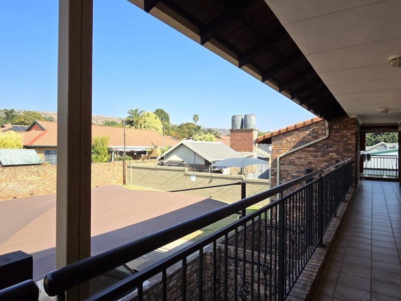 A covered balcony featuring tiled flooring, a wrought iron balustrade, and exposed timber rafters, overlooking the surrounding residential complex.