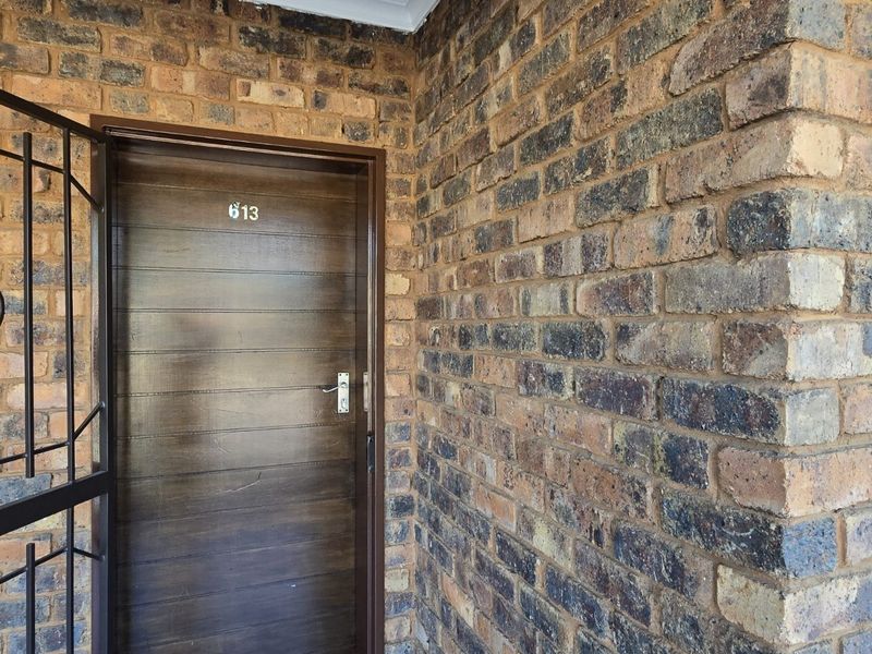 The apartment entrance features a solid wood front door protected by a black metal security gate, set against a face brick exterior wall.