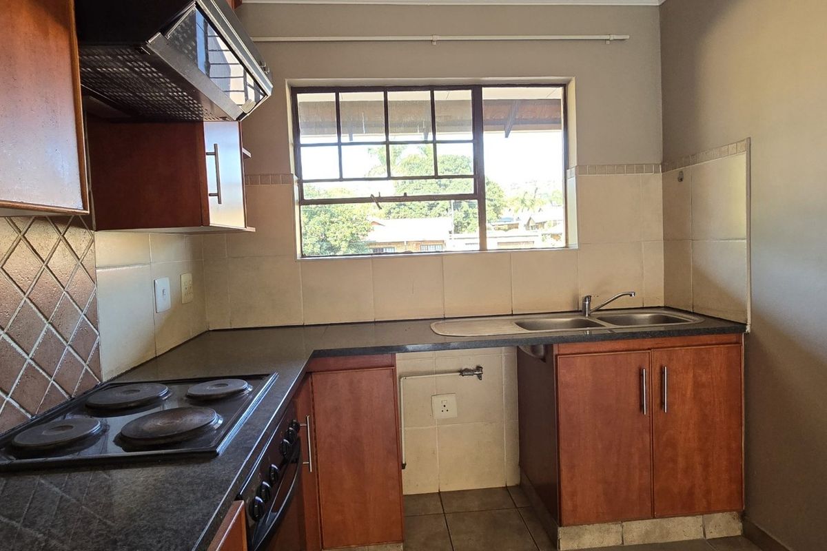 A functional kitchen featuring wood-finish cabinetry, dark laminate countertops, an electric hob with extractor, and a double sink with tiled backsplash.