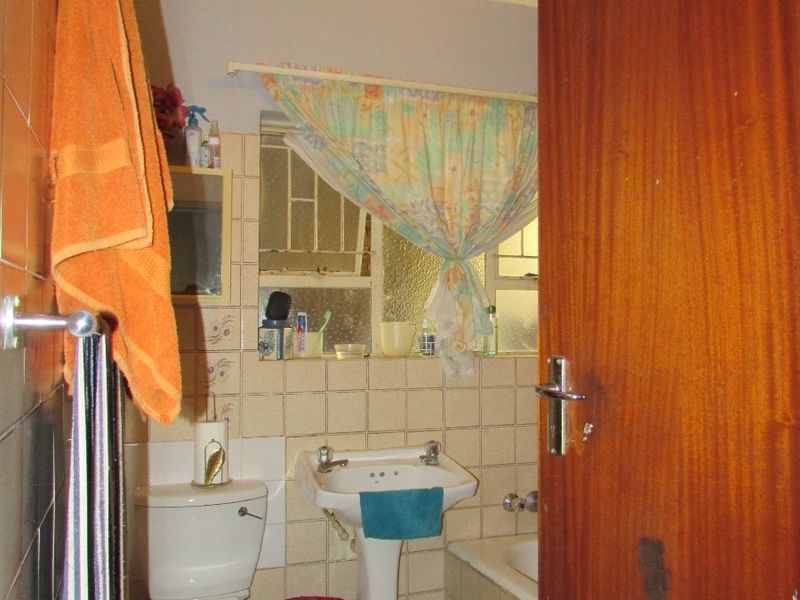 A compact bathroom featuring a pedestal basin, toilet, and bathtub with dated wall tiling and a wooden door.
