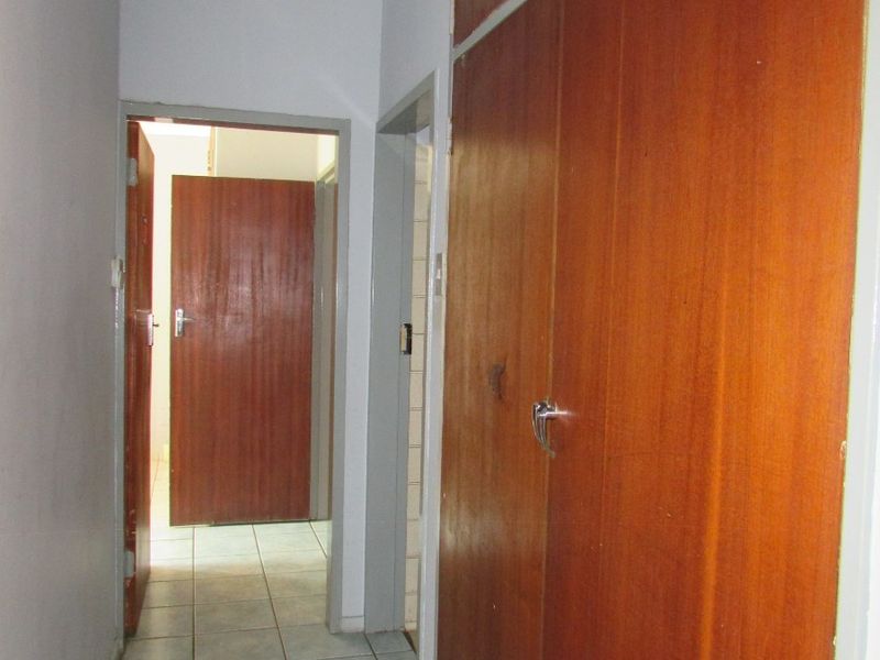 A functional hallway featuring tiled flooring and extensive built-in wooden cupboards, providing ample storage space throughout the corridor.